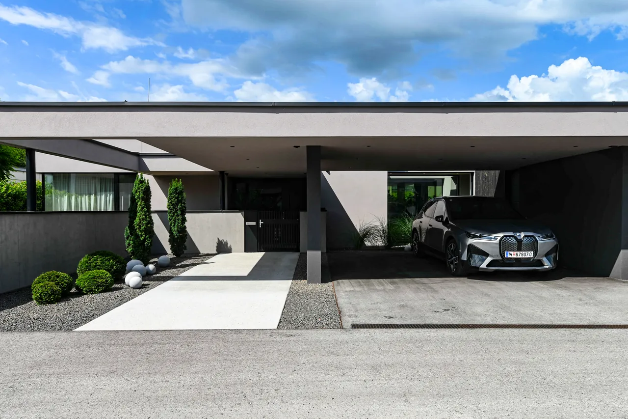 Haus L: Eingangsfassade des Bungalows von aim architektur mit auskragendem Flachdach und Carport